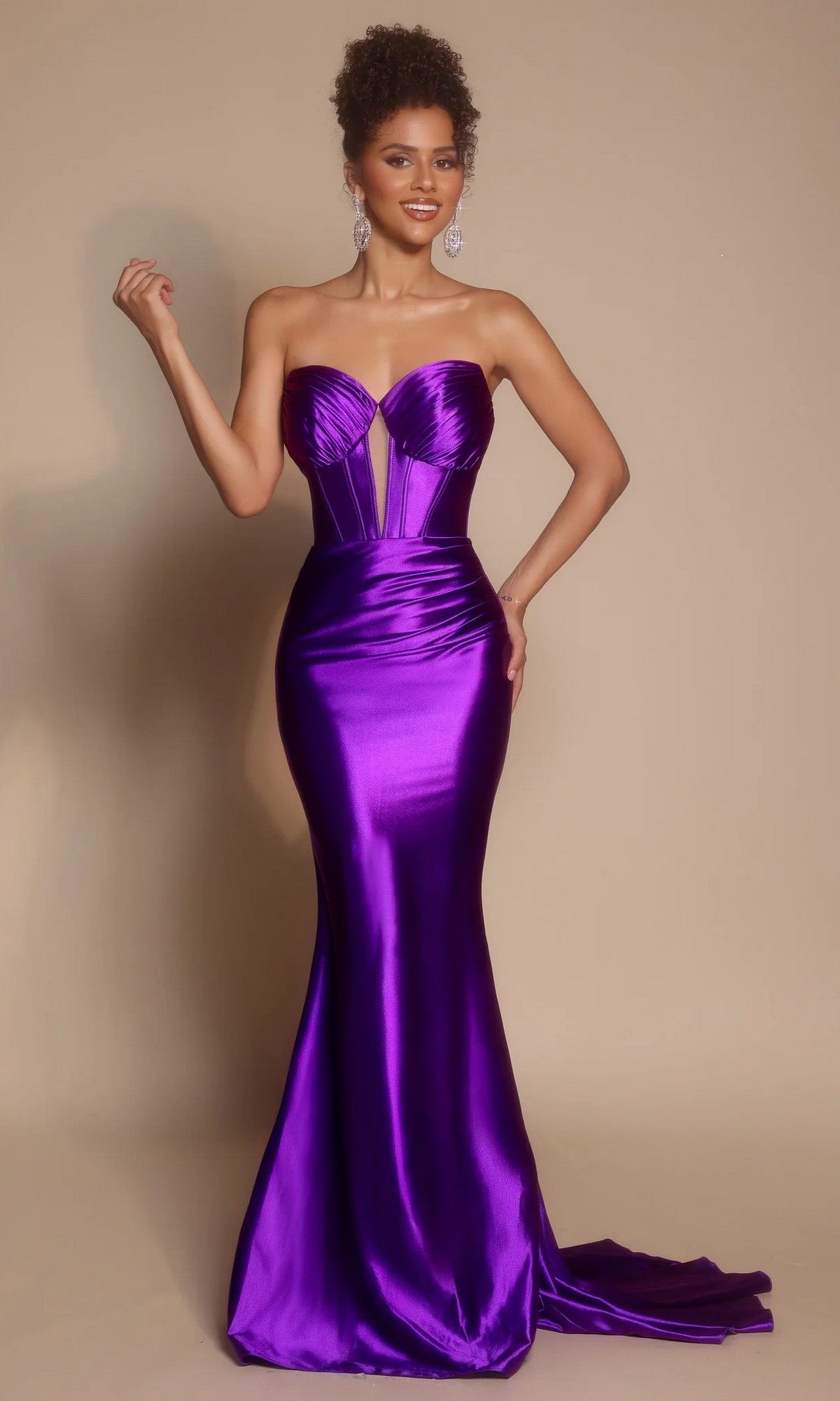 A woman stands against a plain background wearing the Portia and Scarlett XO080 long prom dress in orchid, featuring a strapless satin design with a fitted mermaid silhouette and corset bodice.